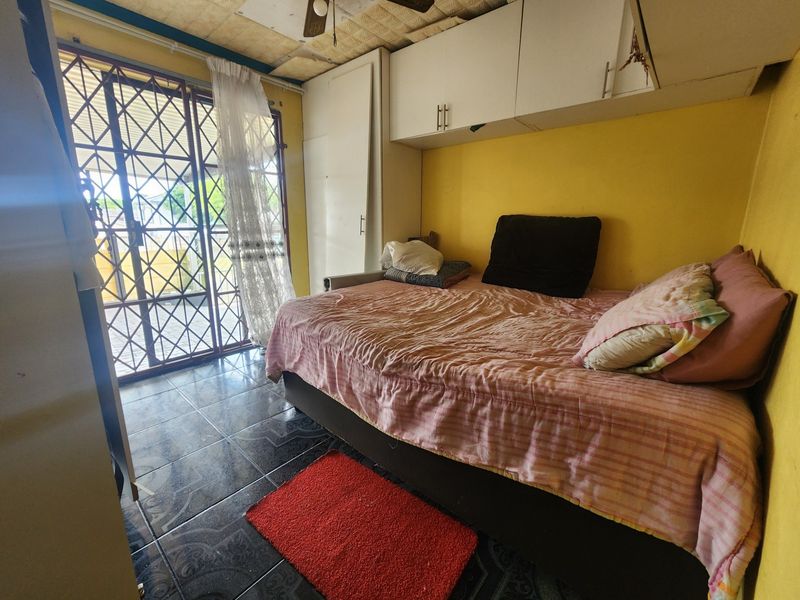 Bedroom featuring tiled flooring, built-in cupboards, and a security gate leading to the exterior. The room requires cosmetic updates to improve its overall condition.