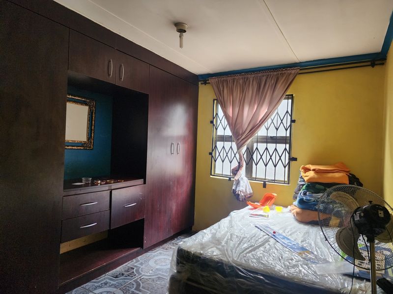 A bedroom featuring built-in dark wood cupboards, tiled flooring, and a window fitted with a security gate.