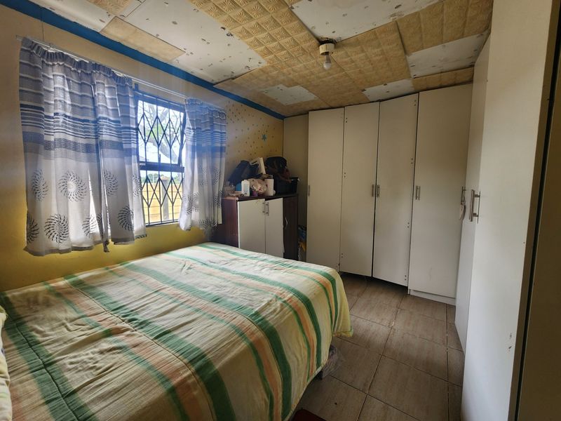 Bedroom featuring built-in cupboards, tiled flooring, and a security gate. The ceiling requires maintenance and repair to improve the overall aesthetic.