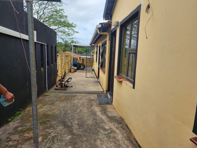 Rear exterior area featuring concrete paving, boundary walls, and access to the side of the house with aluminium window frames.