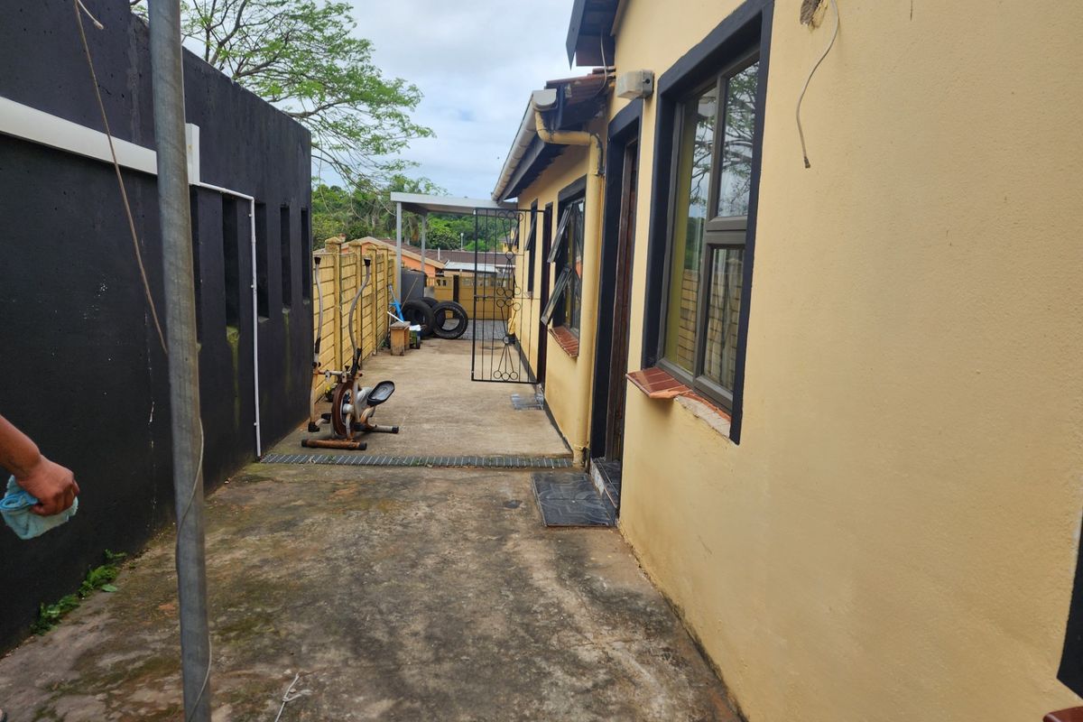 Rear exterior area featuring concrete paving, boundary walls, and access to the side of the house with aluminium window frames.