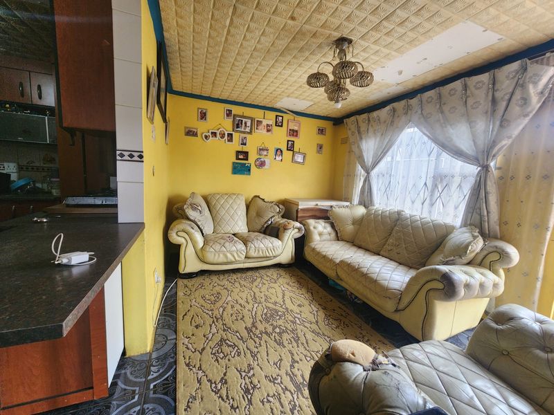 Open plan living area featuring textured ceiling tiles, tiled flooring, and an integrated kitchen counter, requiring cosmetic updates to improve the overall condition.