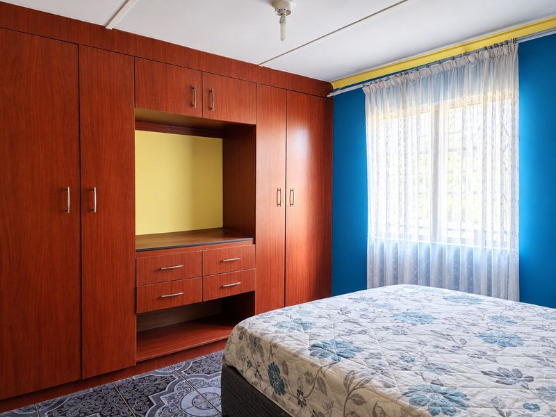 A bedroom featuring extensive built-in wooden cabinetry and a window with security bars, finished with patterned floor tiles.