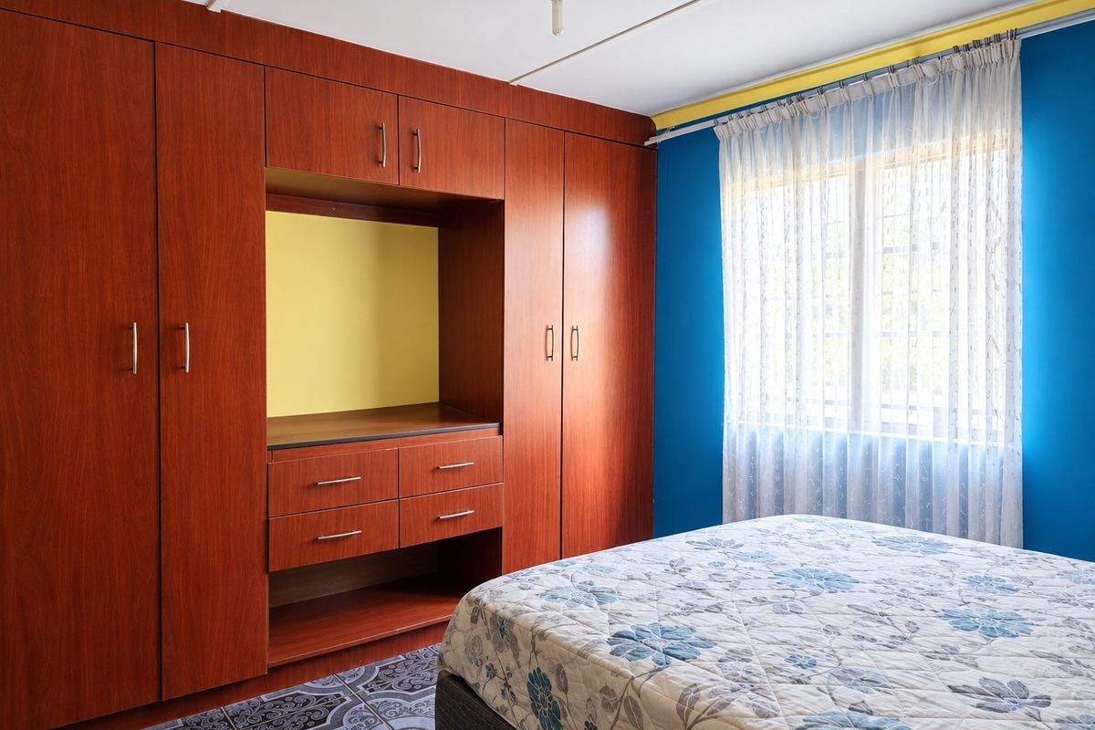 A bedroom featuring extensive built-in wooden cabinetry and a window with security bars, finished with patterned floor tiles.
