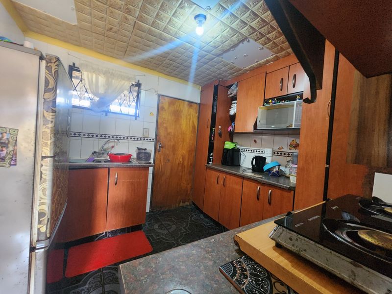 A dated kitchen featuring wooden cabinetry, laminate countertops, and a tiled backsplash, requiring cosmetic updates to modernize the space.