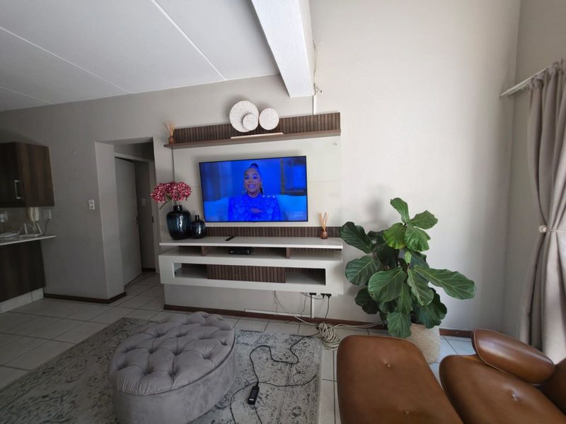 A living room featuring a built-in media console and tiled flooring, with visible wall imperfections and exposed wiring.