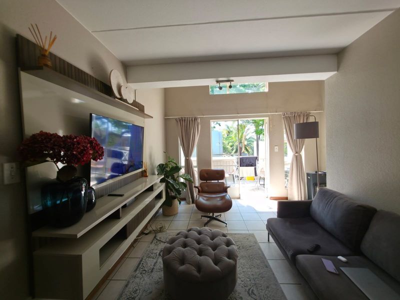 A well-lit living room featuring a built-in media unit, tiled flooring, and a sliding glass door leading to an outdoor patio area.