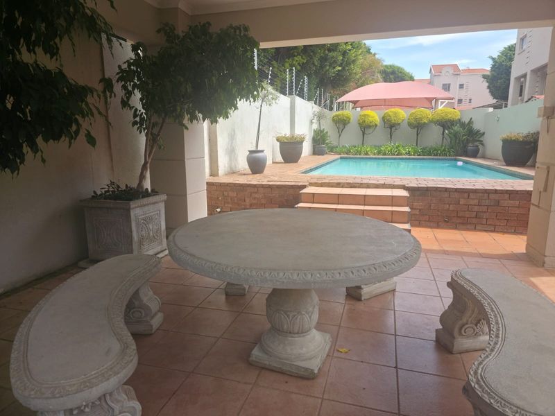 A covered patio area overlooking a private swimming pool with brick coping and landscaped garden borders.