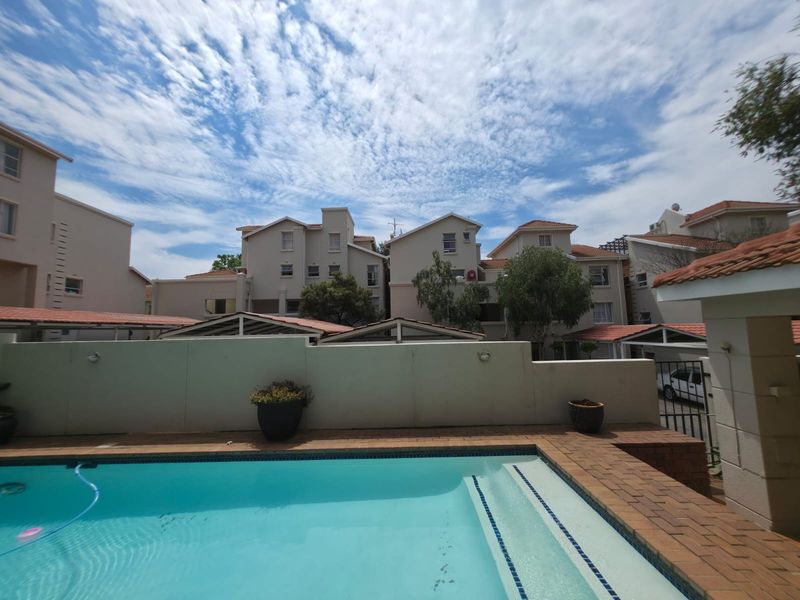 A well-maintained swimming pool area featuring brick paving and a surrounding boundary wall, set within a residential apartment complex.