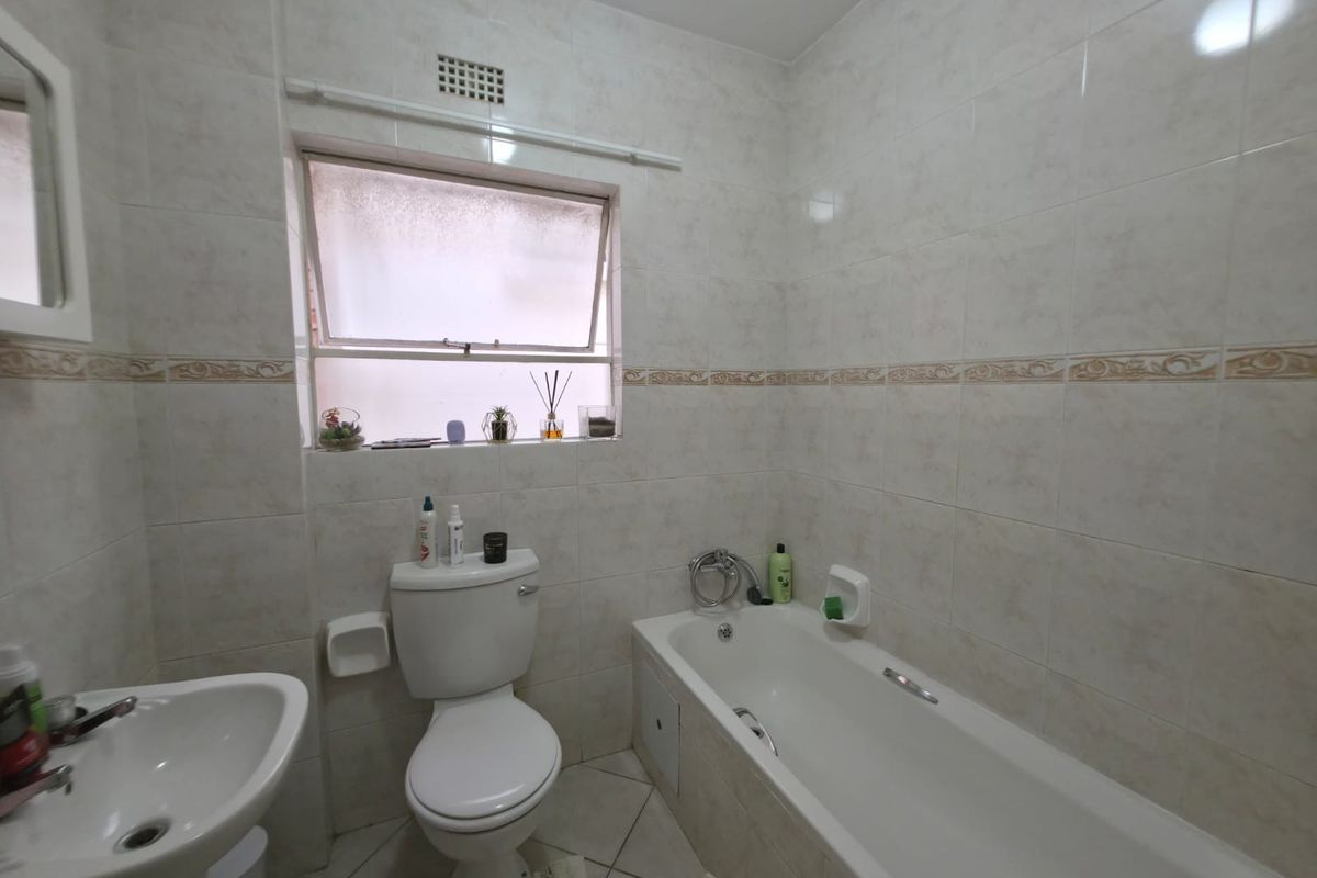 A functional bathroom featuring a pedestal basin, toilet, and bathtub with neutral wall and floor tiling and a top-hung window for ventilation.