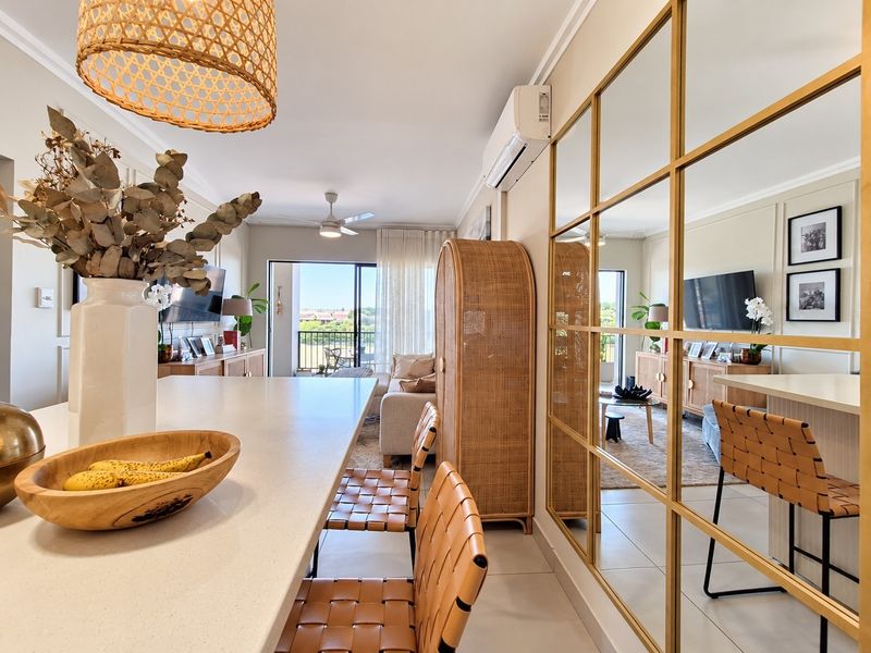 Modern open-plan living area featuring a stone kitchen island, mirrored feature wall, split-system air conditioning, and seamless access to a private balcony.