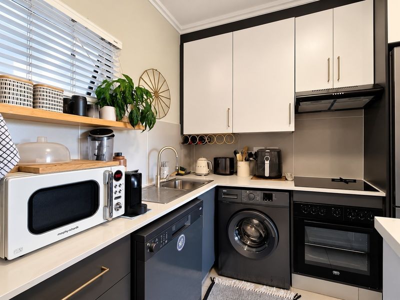 Modern kitchen featuring sleek two-tone cabinetry, stone countertops, integrated oven, electric hob, extractor fan, and a stainless steel sink with a contemporary mixer tap.