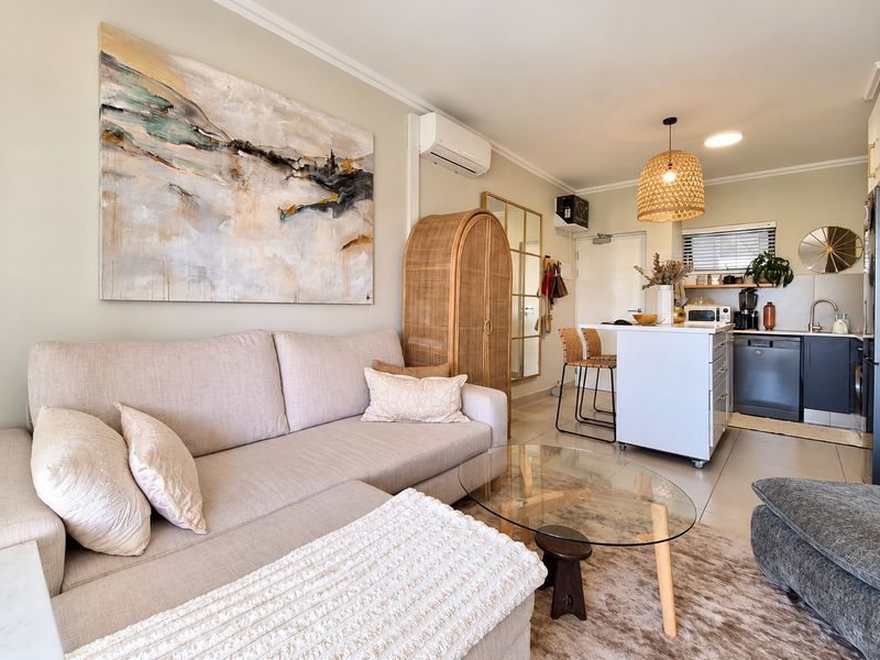 A well-presented open-plan living and kitchen area featuring tiled flooring, a modern kitchen island with integrated dishwasher, and a split-system air conditioner.