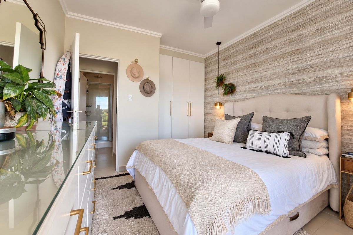 A well-maintained bedroom featuring built-in cupboards, a ceiling fan, and a textured feature wall, with direct access to an en-suite bathroom.