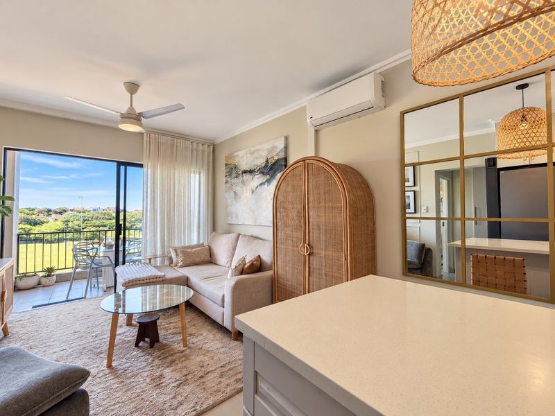 Modern open-plan living area featuring a stone-topped kitchen island, split-system air conditioning, ceiling fan, and seamless access to a private balcony with scenic views.