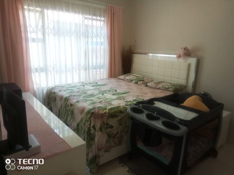 A functional bedroom featuring tiled flooring and a large sliding window with integrated security gate, providing natural light to the space.