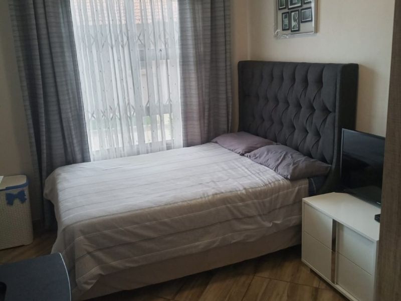A cozy bedroom featuring tiled flooring and a window equipped with a security gate, providing a functional and well-maintained living space.