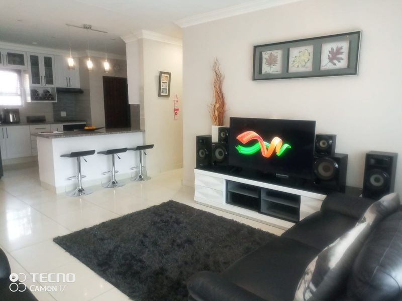An open-plan living area featuring a modern kitchen with granite countertops and tiled flooring, seamlessly flowing into a comfortable lounge space.
