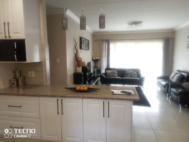 An open-plan living and kitchen area featuring white cabinetry, granite countertops, tiled flooring, and modern lighting fixtures, creating a bright and functional living space.