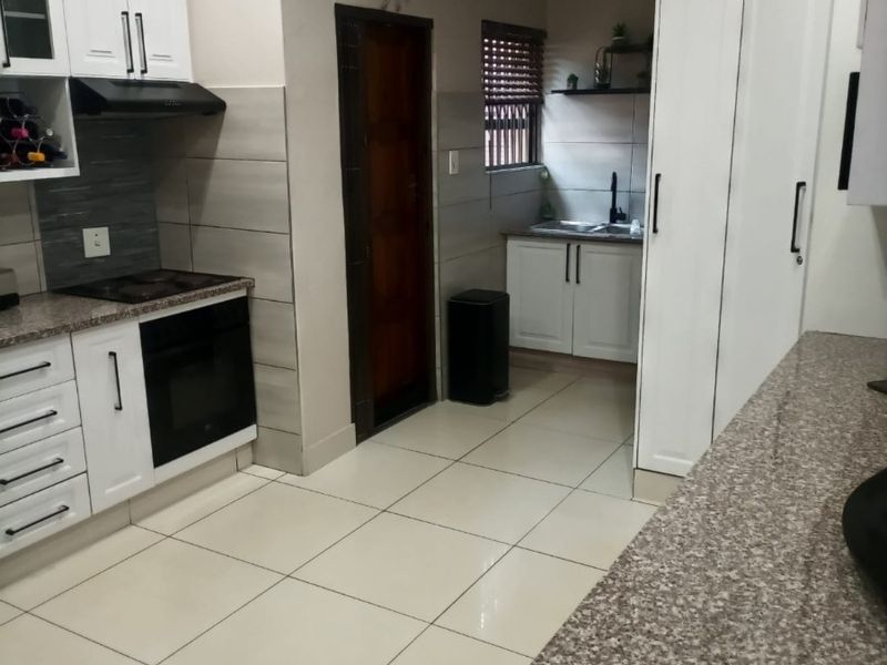 Modern kitchen featuring white cabinetry, granite countertops, built-in oven and hob, extractor fan, and tiled flooring with a functional layout.