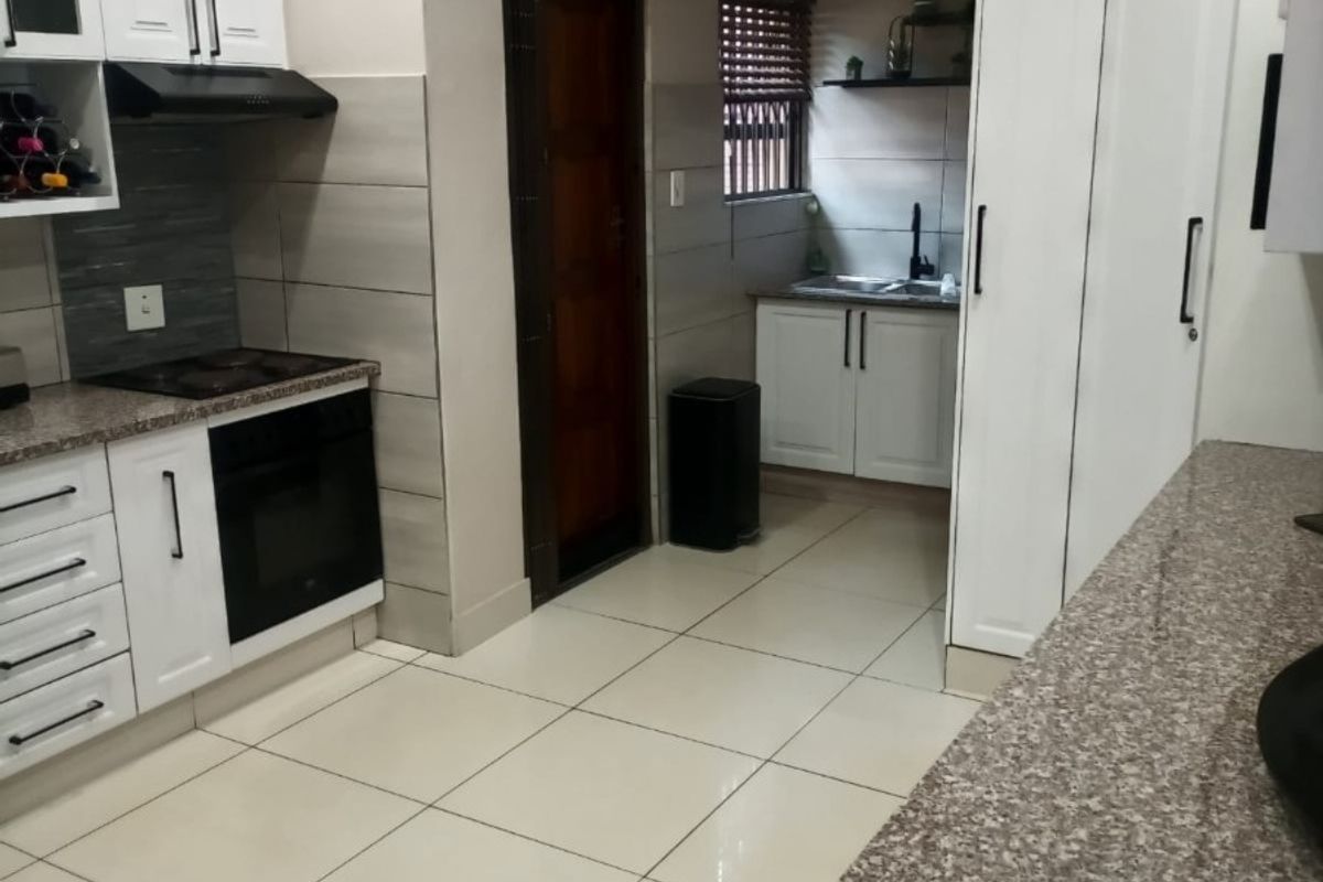Modern kitchen featuring white cabinetry, granite countertops, built-in oven and hob, extractor fan, and tiled flooring with a functional layout.