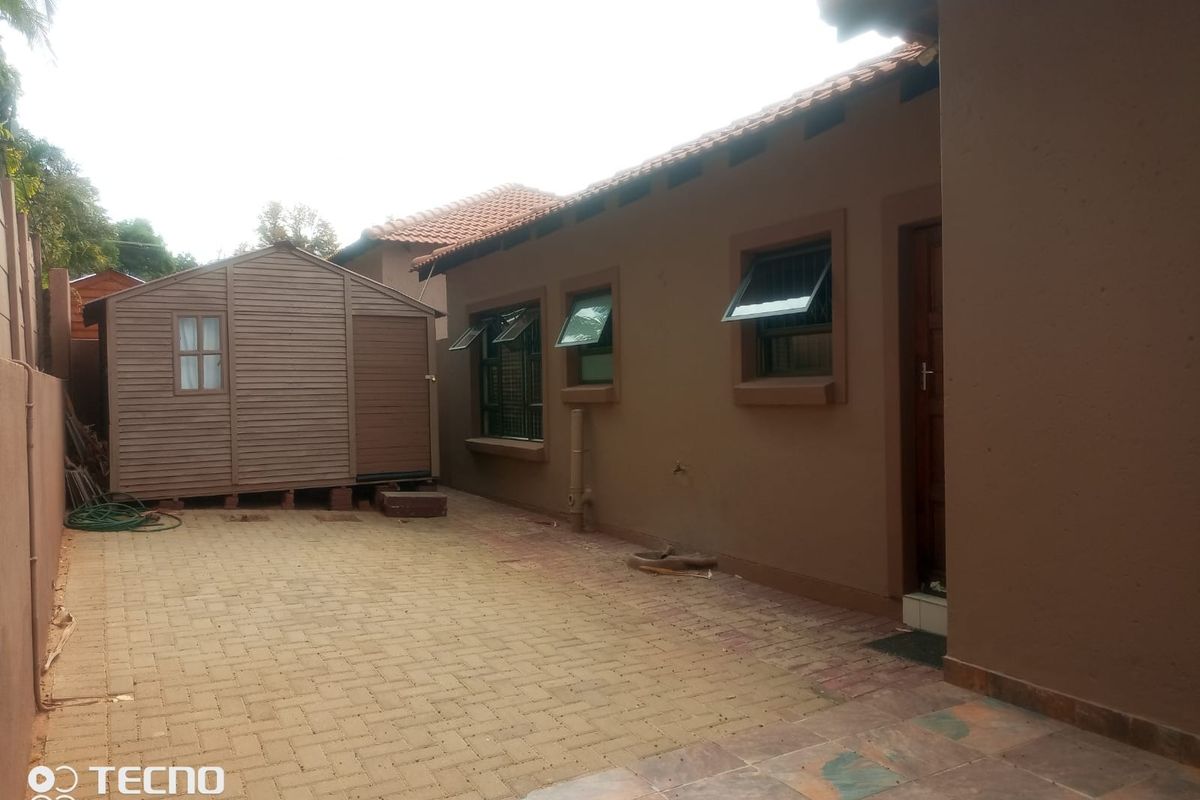 A rear exterior view of the property featuring a paved courtyard, a timber storage shed, and a tiled roof structure.
