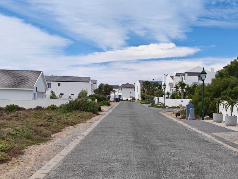 A clear street view of a residential estate featuring paved roads, sidewalks, and established boundary walls with surrounding landscaping.