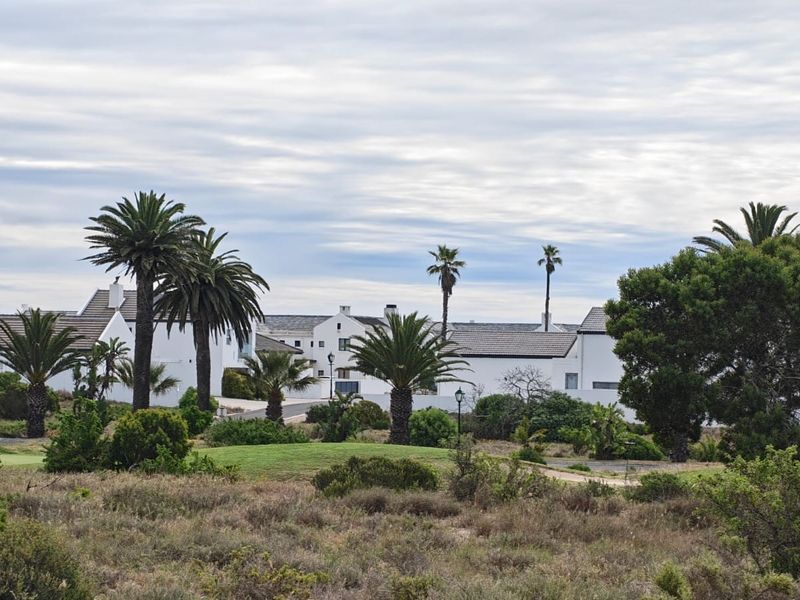 A scenic view of a residential estate featuring well-maintained gardens, mature palm trees, and white architectural structures under a cloudy sky.