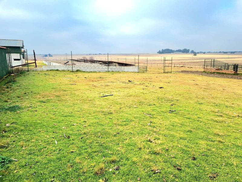 Expansive farm land featuring wire fencing, a concrete block wall, and an outbuilding structure set against an open rural landscape.