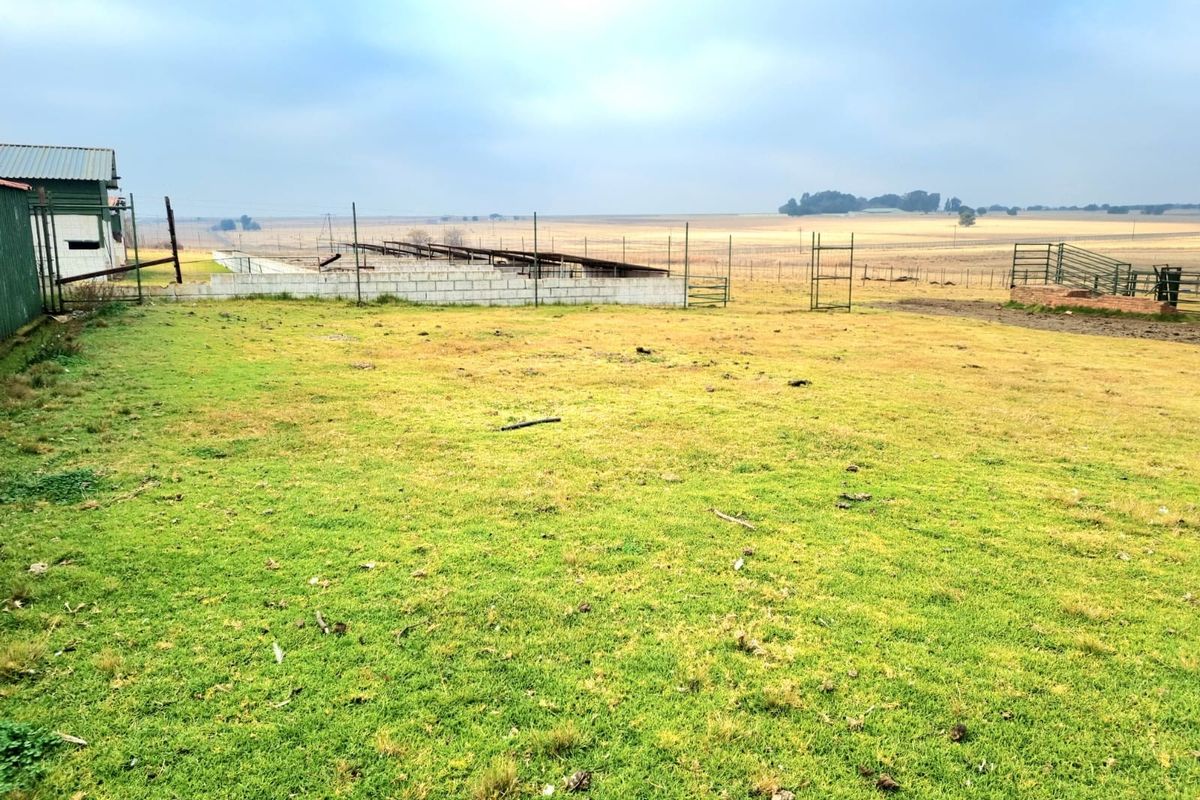 Expansive farm land featuring wire fencing, a concrete block wall, and an outbuilding structure set against an open rural landscape.