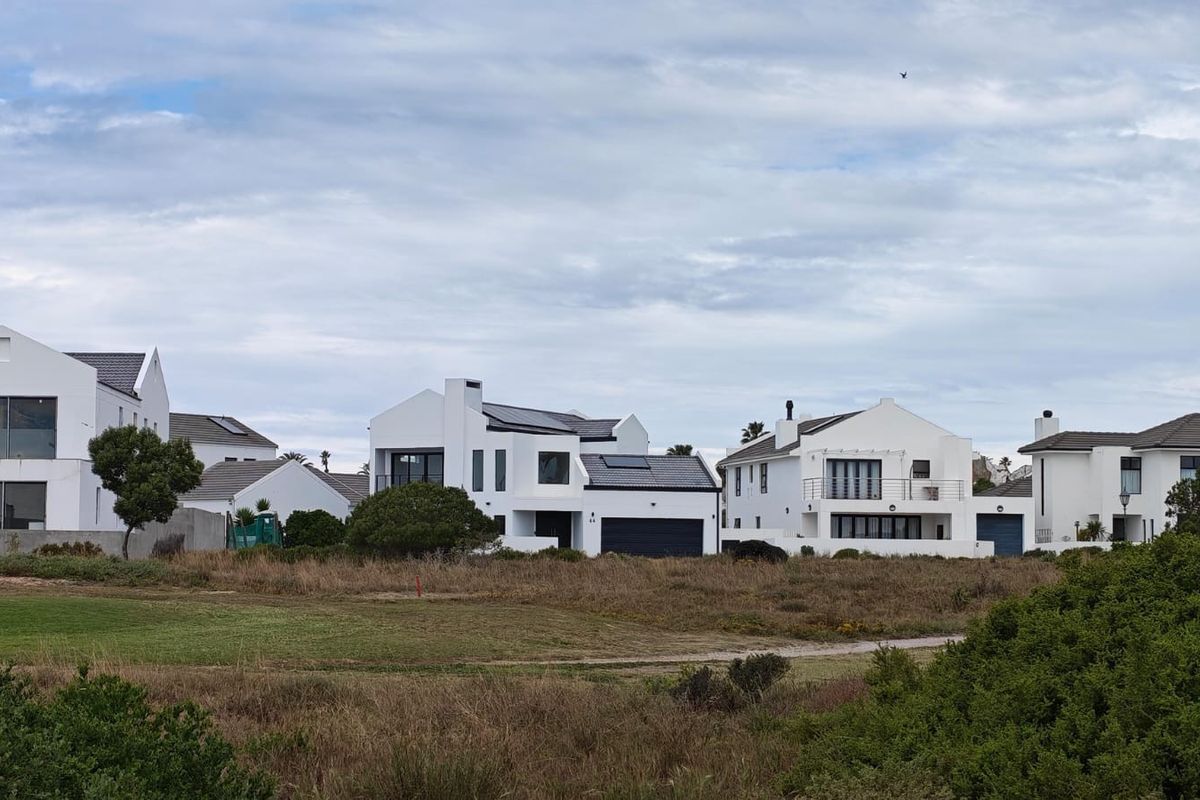 A view of modern residential homes with white facades, tiled roofs, and solar panels, situated adjacent to an open natural landscape.