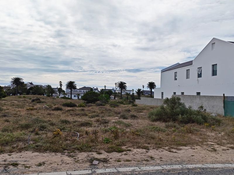 A view of a vacant residential plot of land adjacent to an existing white multi-story residential building.