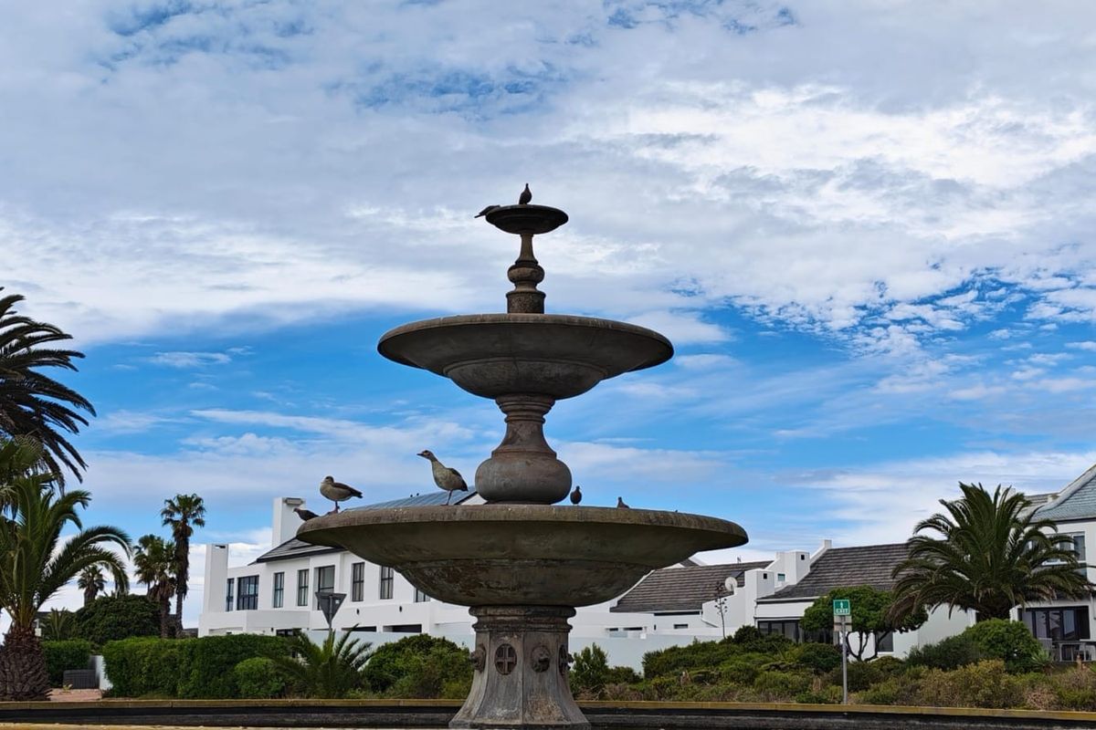 A decorative stone fountain centerpiece situated within a landscaped garden area, featuring tiered basins and surrounding greenery.
