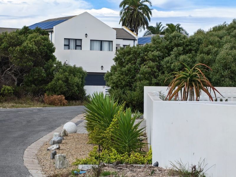 A street-level view of a residential property featuring a paved driveway, boundary wall, and a well-maintained garden with solar panels visible on the roof.