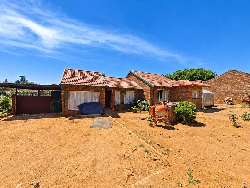 Rear view of a face brick house featuring a tiled roof and an attached carport, set on a large, unlandscaped plot.