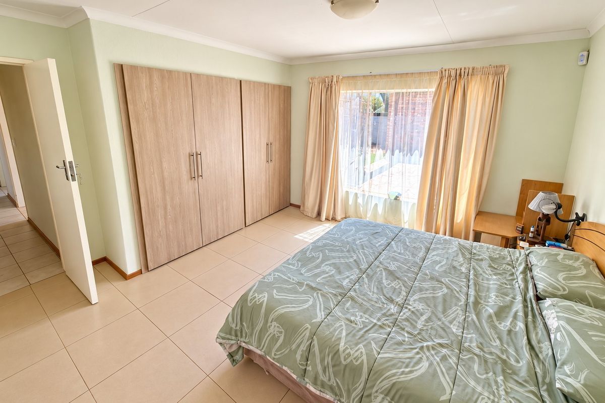 A well-maintained bedroom featuring neutral tiled flooring, built-in wooden cupboards, and natural light through a large window.