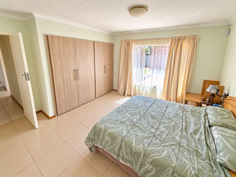 A well-maintained bedroom featuring neutral tiled flooring, built-in wooden cupboards, and natural light through a large window.