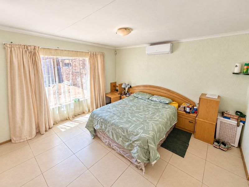 Spacious bedroom featuring tiled flooring, a wall-mounted air conditioning unit, and large windows allowing for natural light.