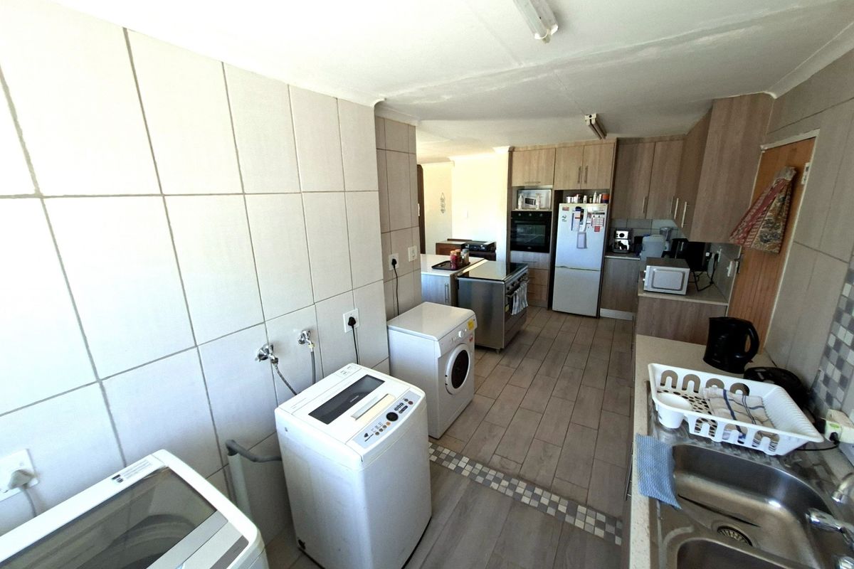 A functional kitchen and laundry area featuring tiled flooring, ample built-in cabinetry, a double sink, and integrated oven with extractor fan.