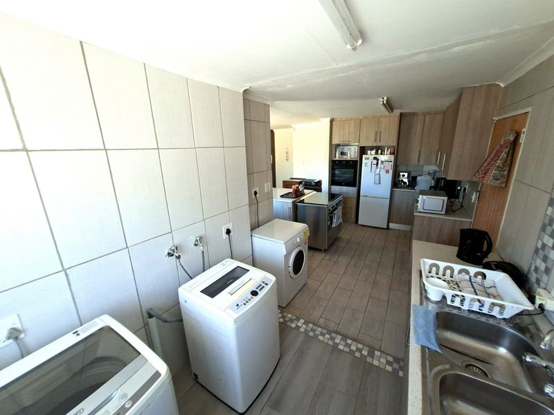 A functional kitchen and laundry area featuring tiled flooring, ample built-in cabinetry, a double sink, and integrated oven with extractor fan.