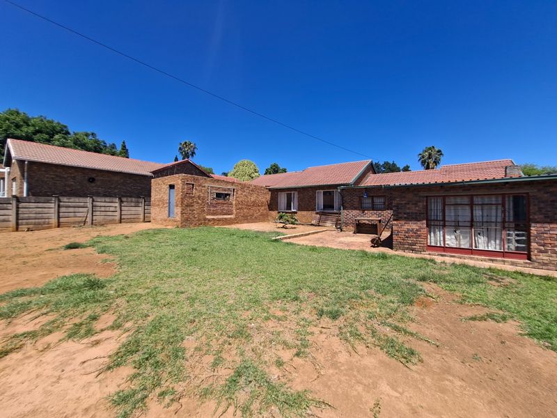 Rear view of a face brick house featuring a tiled roof, sliding glass doors, and a spacious backyard with a paved patio area.