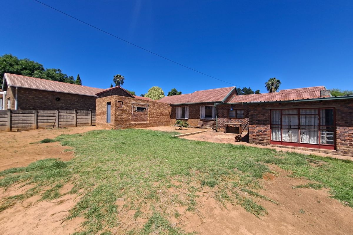Rear view of a face brick house featuring a tiled roof, sliding glass doors, and a spacious backyard with a paved patio area.