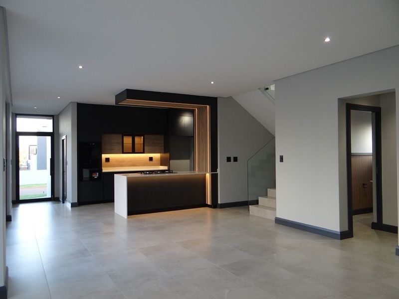 Modern open-plan living area featuring a sleek kitchen with built-in appliances, island, and contemporary finishes, adjacent to a staircase with glass balustrades.