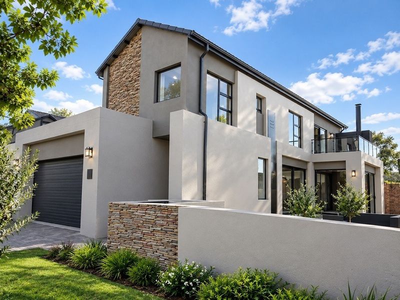 Modern double-storey residence featuring contemporary stone cladding, a spacious garage, and a private balcony with glass balustrades, set within a well-maintained landscaped garden.