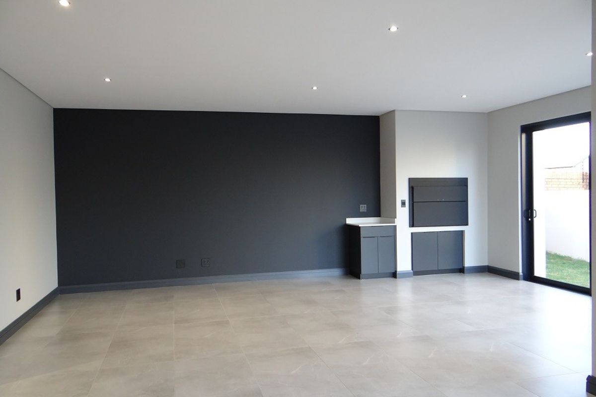 Spacious open-plan living area featuring modern tiled flooring, recessed downlights, a built-in braai, and direct access to the garden through a sliding glass door.
