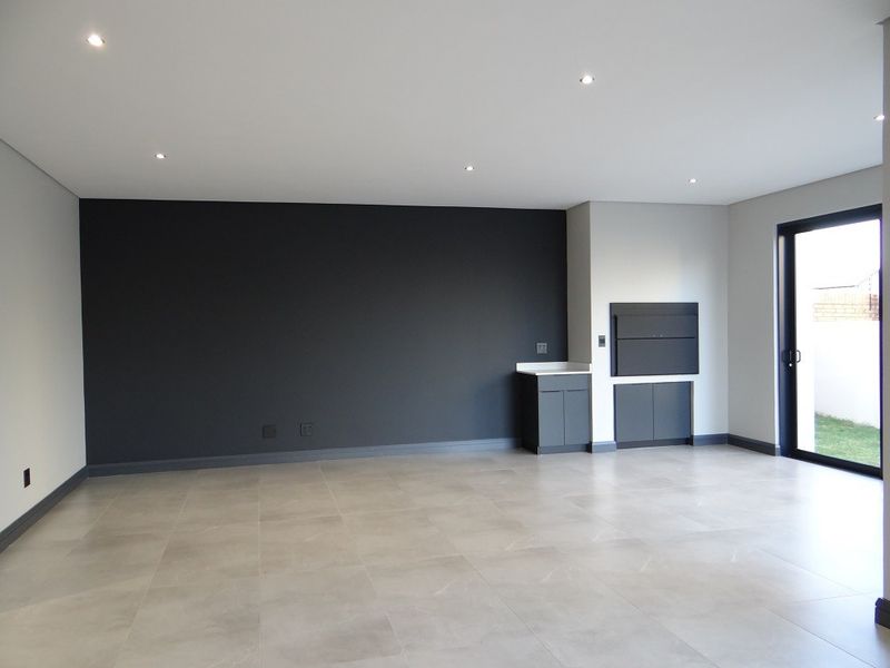 Spacious open-plan living area featuring modern tiled flooring, recessed downlights, a built-in braai, and direct access to the garden through a sliding glass door.