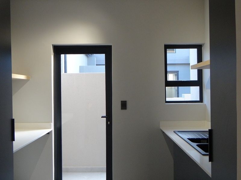 A modern, minimalist scullery featuring sleek cabinetry, stone countertops, an integrated sink, and direct access to an outdoor area.