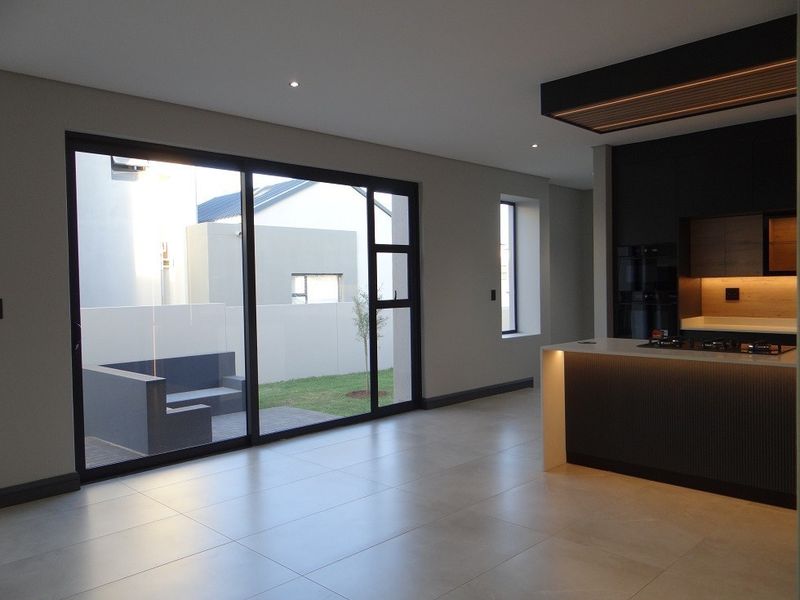 Modern open-plan living area featuring a sleek kitchen island with built-in hob, large sliding glass doors, and neutral tiled flooring.