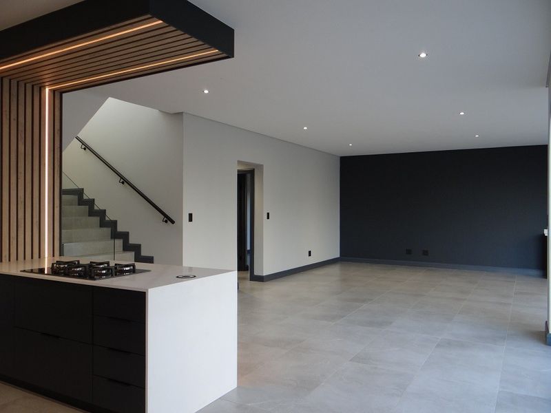Modern open-plan living area featuring a sleek kitchen island with gas hob, tiled floors, and a striking timber slat ceiling detail above the kitchen.