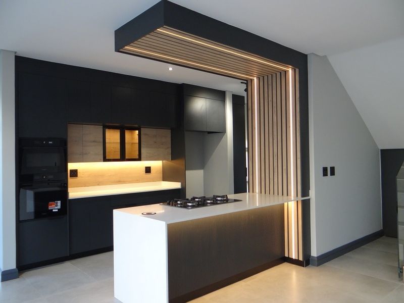 Modern kitchen featuring sleek dark cabinetry, stone countertops, a central island with a gas hob, and a striking slatted timber bulkhead with integrated lighting.